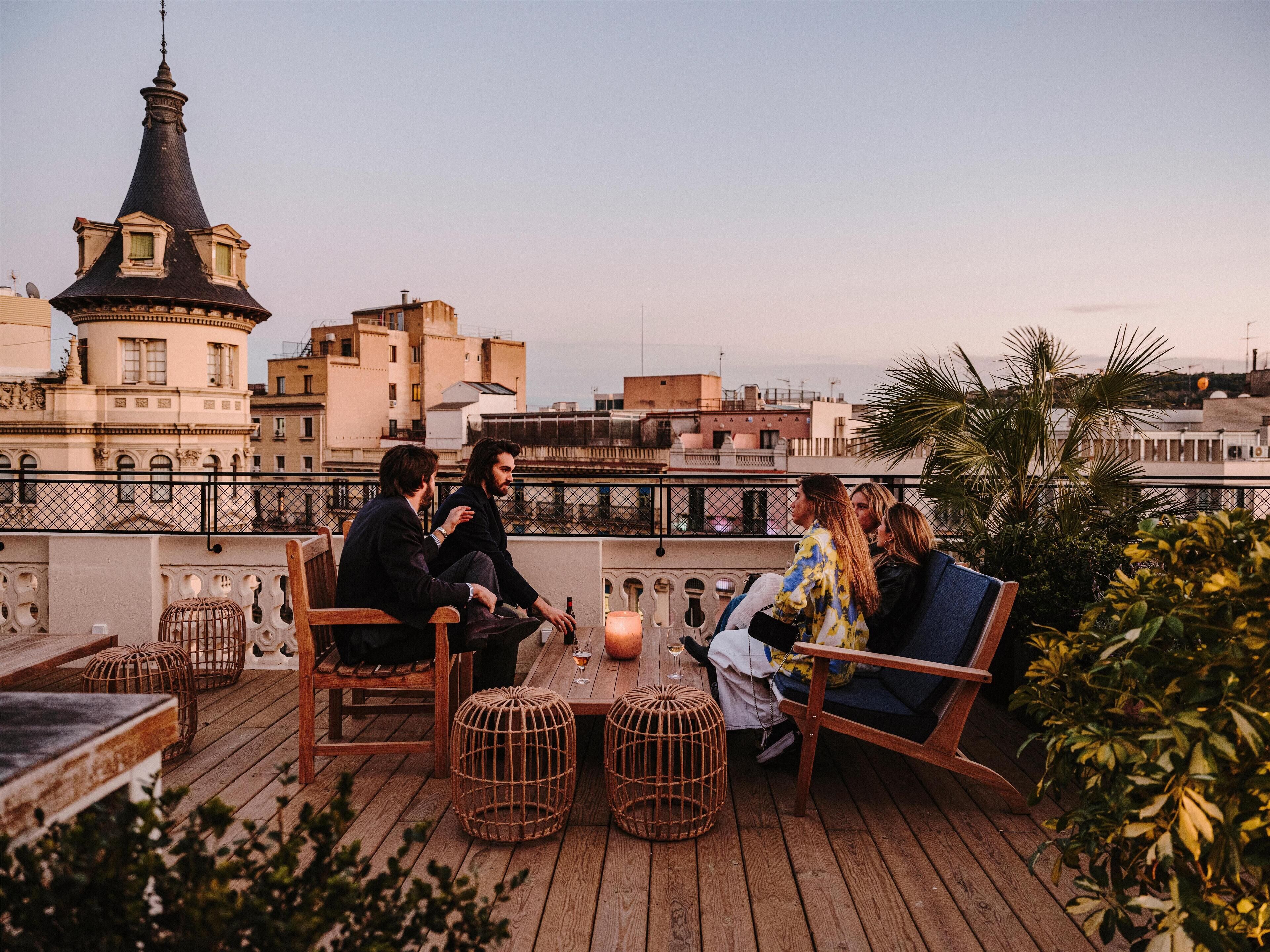 Eine Dachterrasse mit Holzmöbeln, einem Tisch mit Getränken und Blick auf Stadtgebäude.