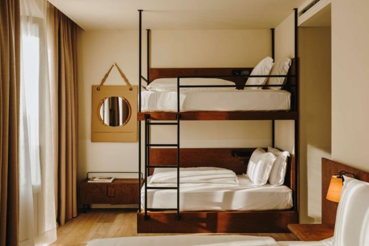 A bunk bed room with a wooden ladder, a bedside table, a hanging mirror, and a lamp.