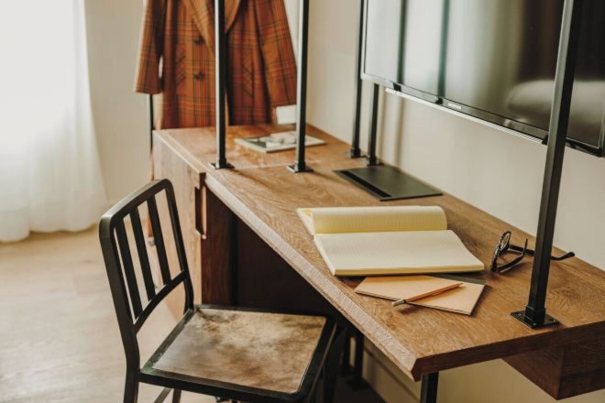 A wooden desk with a chair, a notebook, and a pair of glasses.