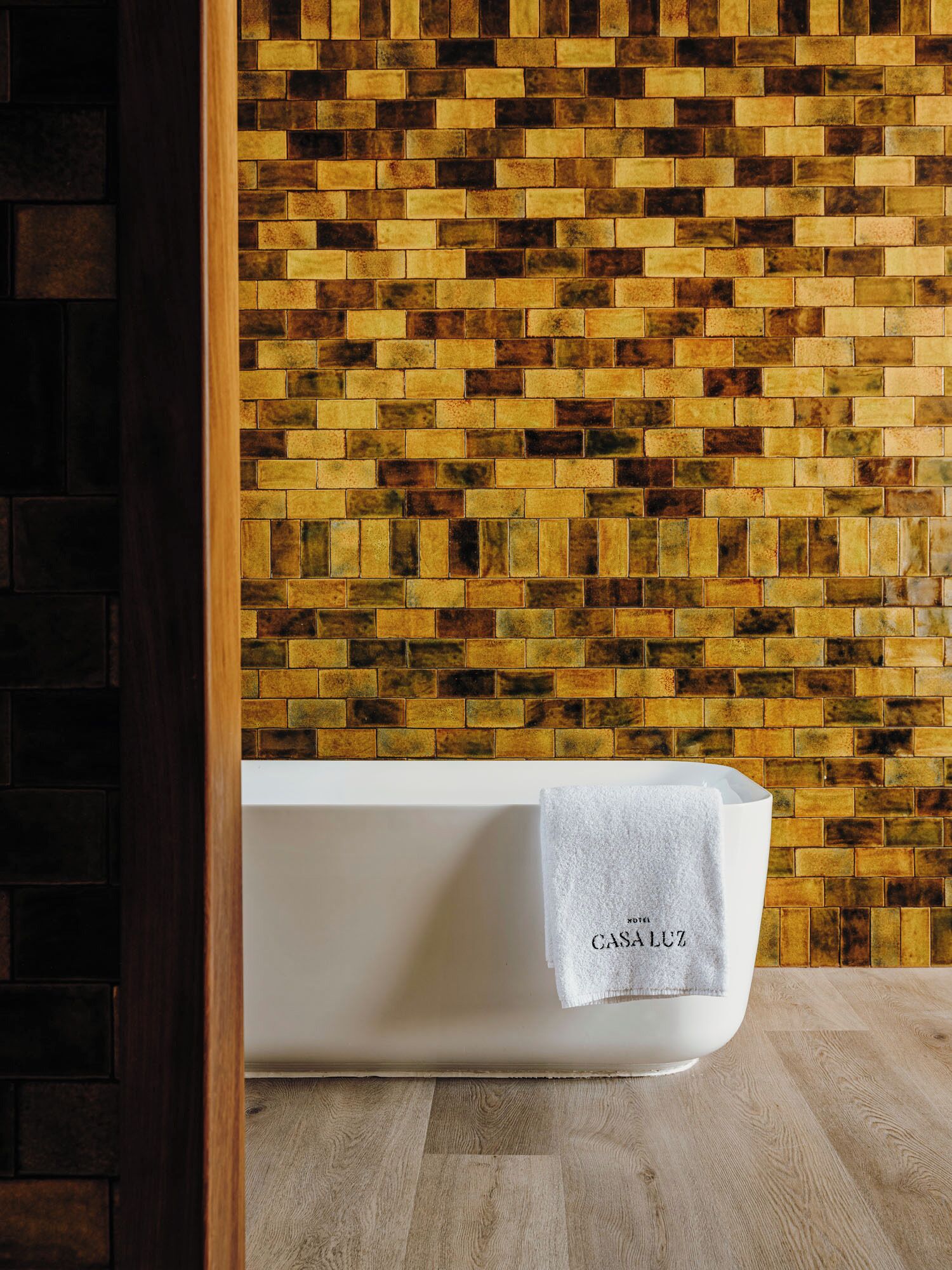 A white bathtub with a towel labeled "CASALUZ" against a mosaic tile wall.