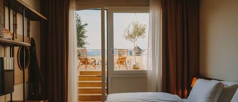 Un dormitorio con cama, escritorio y vistas a un balcón exterior con sillas y una mesa.