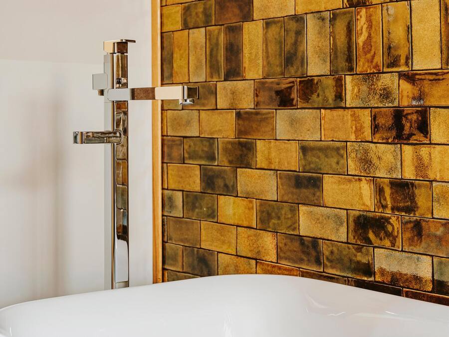 Un baño con una bañera blanca, un grifo de cromo y una pared de azulejos con diseño de ladrillo.