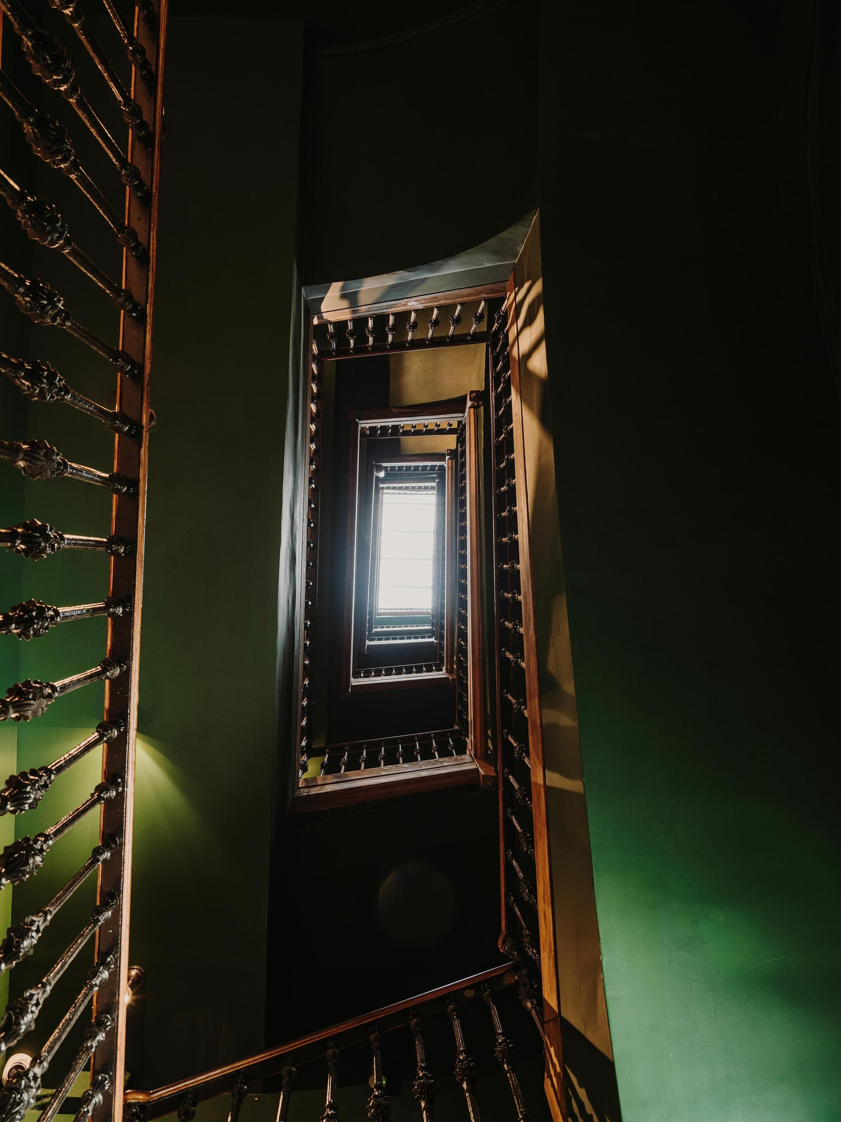 A narrow stairwell with a metal railing and a small window at the top.