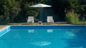 Piscina com duas espreguiçadeiras e um guarda-sol.