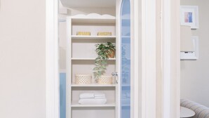 Casa de banho com toucador branco, porta-toalhas e prateleira com produtos de higiene pessoal.