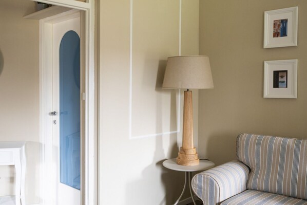 A room with a blue door, a round table with a lamp, a striped sofa, and two framed pictures on the wall.