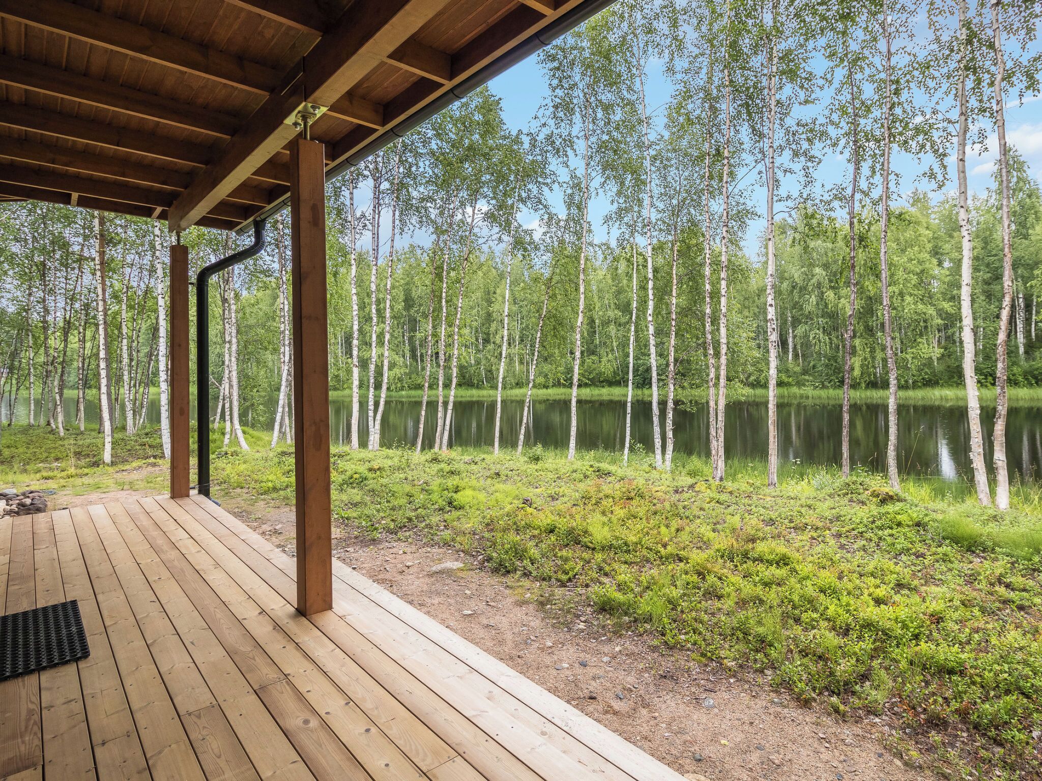 Terraza de madera con vistas a un lago y abedules.