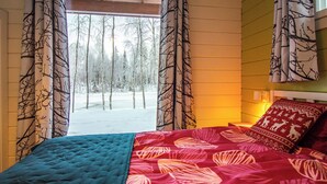 Un dormitorio con cama, ventana con cortinas, vista a un bosque nevado y una pared con almohada estampada.