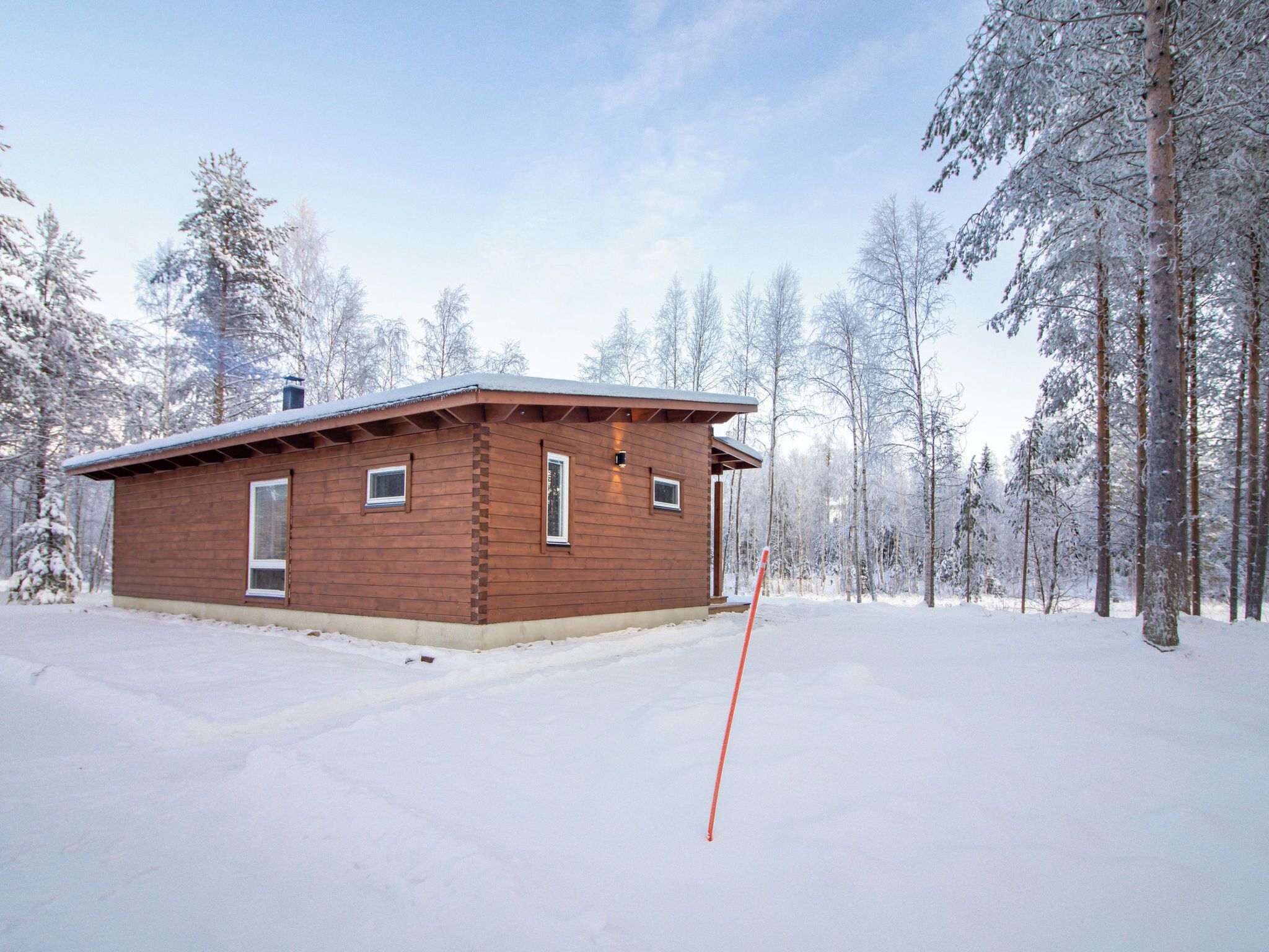 En stuga av trä med ett platt tak, omgiven av snötäckta träd.