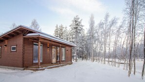Una cabaña de madera con techo nevado, rodeada de un bosque.