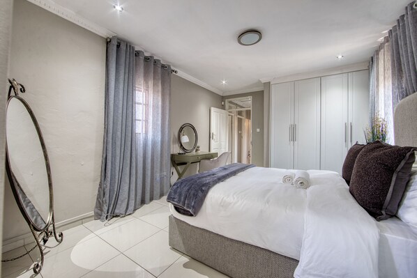 A bedroom with a large bed, a desk, a mirror, and a wardrobe.