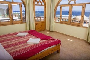 A bedroom with a large bed, wooden windows, and a view of the sea.
