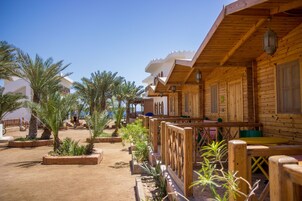 A wooden cabin-style hotel with outdoor seating and palm trees.
