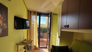Una sala de estar con un sofá verde, un televisor montado en la pared y un comedor con mesa y sillas.