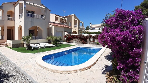 Um edifício de dois andares com piscina, área de estar externa e um jardim bem cuidado.