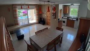Ampla sala de estar com uma grande mesa de jantar, TV e porta de vidro deslizante para um pátio externo.