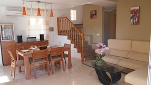 Uma sala de jantar com mesa e cadeiras de madeira, uma mesinha de centro de vidro e uma escada que leva a um andar superior.
