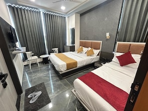 A hotel room with two beds, a desk, a chair, a small table, and a TV. - HOTEL SAWARIYA (Ahmedabad)