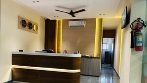 A reception area with a wooden reception desk, a ceiling fan, and a wall-mounted air conditioning unit. - HOTEL SAWARIYA (Ahmedabad)