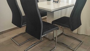 A conference room with a white table, four black chairs with metal frames, a potted plant, and a picture frame. - Modern 2BR Apartment In Prime Vienna (Vienna)