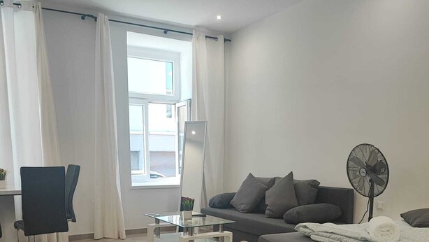A modern living room with a sofa, a coffee table, a chair, and a standing fan. - Modern 2BR Apartment In Prime Vienna (Vienna)