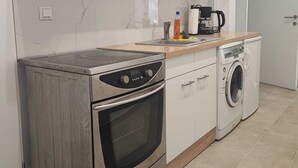 A compact kitchen with a built-in oven, a microwave, a washing machine, and a coffee maker. - Modern 2BR Apartment In Prime Vienna (Vienna)