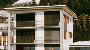 Ein modernes, mehrstöckiges Gebäude mit Balkonen und großen Fenstern, umgeben von Schnee und Bäumen.