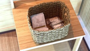 Cesto intrecciato con confezione di prodotto etichettata 'AURA Luxury Collection' e un oggetto più piccolo, su una superficie in legno.