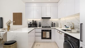 A modern kitchen with white cabinetry, a built-in oven, a dishwasher, and a coffee maker. - Close to Community Park, Minutes Walk from Circle Mall, and Short Drive to Dubai Miracle Garden (Dubai)