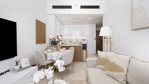 A modern living room with a sofa, a dining table, and a kitchen in the background. - Close to Community Park, Minutes Walk from Circle Mall, and Short Drive to Dubai Miracle Garden (Dubai)