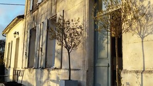 Un edificio de dos pisos con un estilo arquitectónico clásico, que presenta ventanas simétricas y una entrada central con puerta.