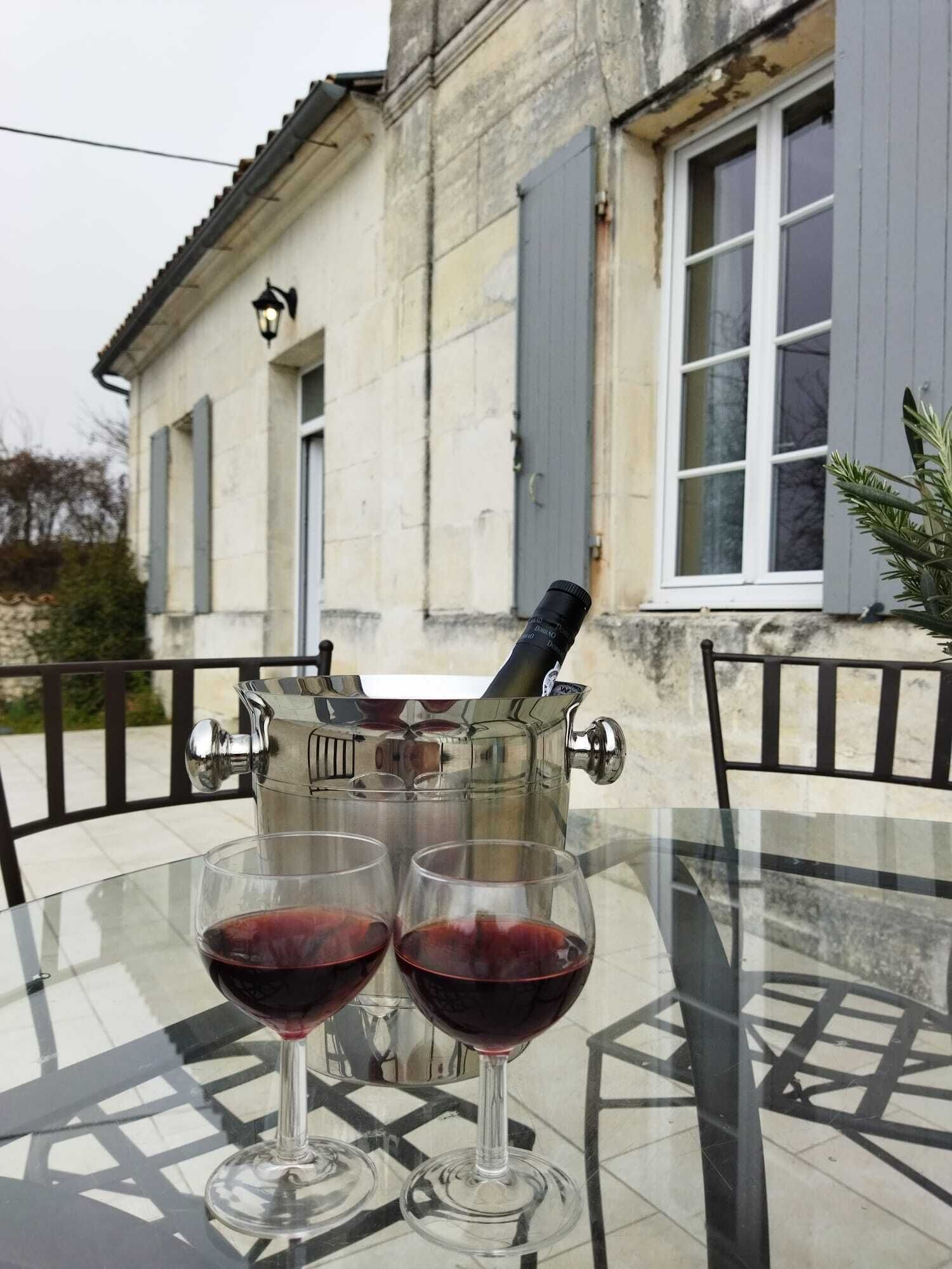Ein Glastisch mit zwei Weingläsern, gefüllt mit Rotwein, einer Champagnerflasche und einem Metall-Eisbecher.