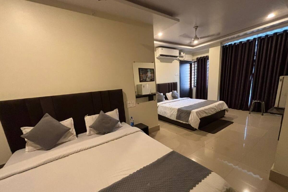 Une chambre d’hôtel avec deux lits, un ventilateur de plafond, un appareil de climatisation, une fenêtre avec des rideaux et un petit tabouret.