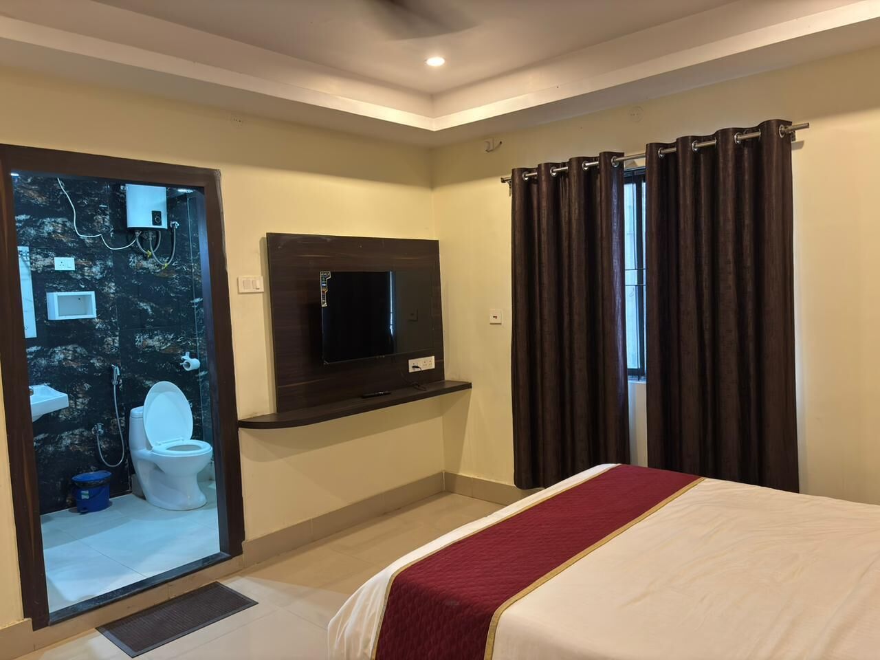 A hotel room with a bed, a television, a mirror, and a bathroom visible through an open door.