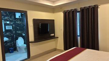 A hotel room with a bed, a television, a mirror, and a bathroom visible through an open door.