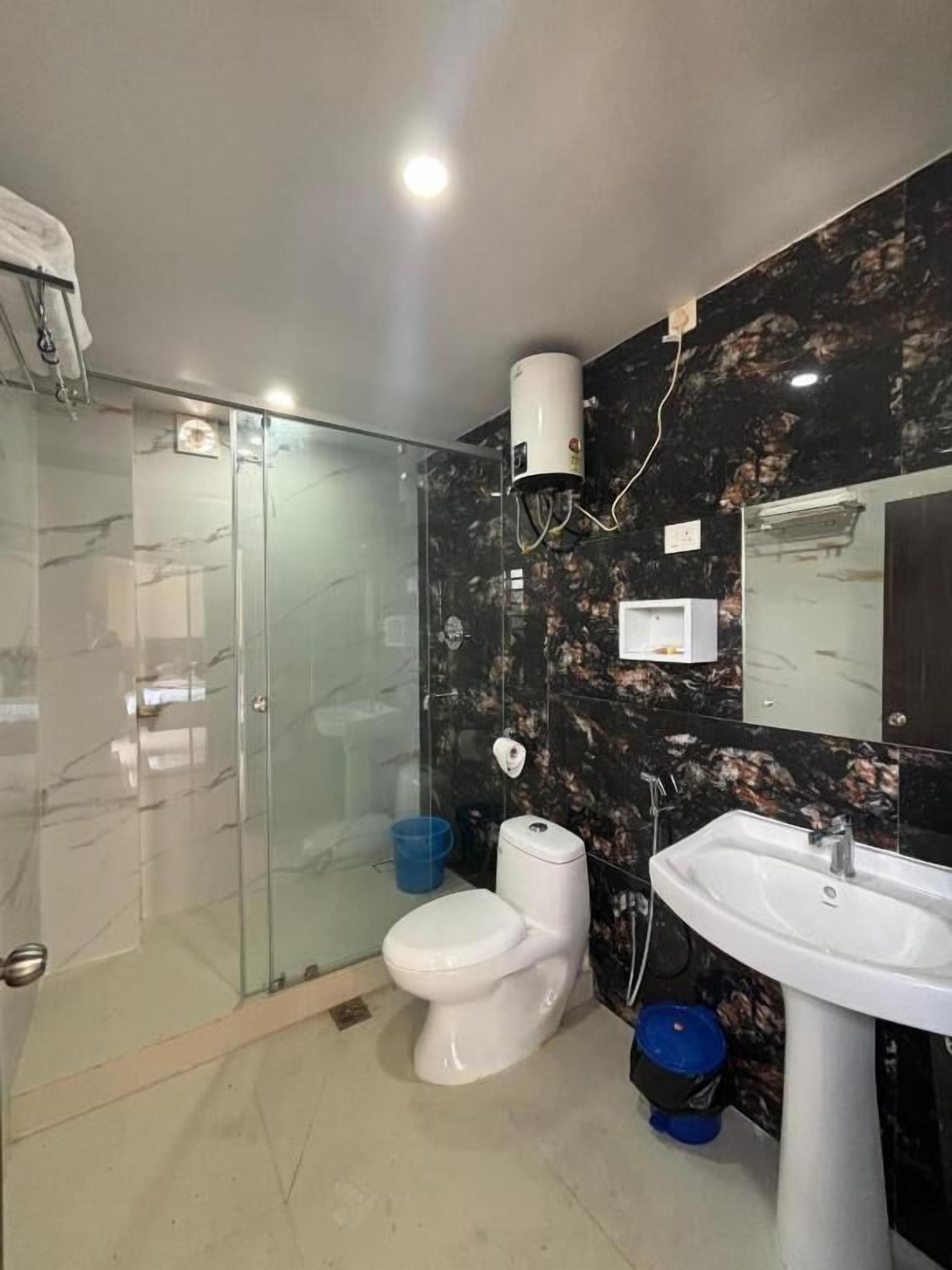 Baño con ducha envuelta en vidrio, inodoro, lavamanos y pared con diseño de mármol.