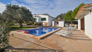 Una piscina con sillones de descanso, un patio y un edificio blanco con techo de tejas.