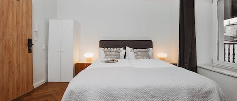 A neatly arranged bedroom with a bed, bedside lamps, a wardrobe, and a window with curtains.