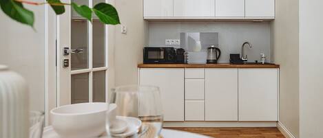 Una cocina moderna con armarios blancos, microondas, cafetera y fregadero.