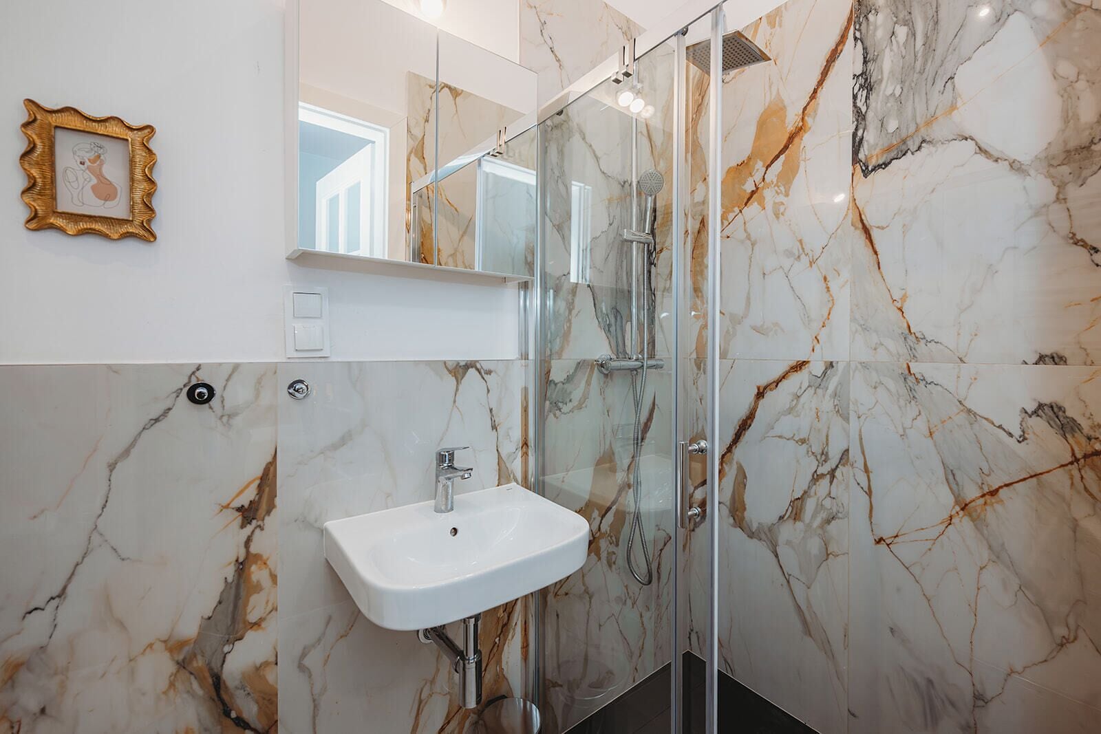 Une salle de bain avec un mur en marbre, une douche en verre et un lavabo blanc.