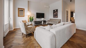 Ein Wohnzimmer mit Sofa, Sessel, Fernseher und einem Bild an der Wand.