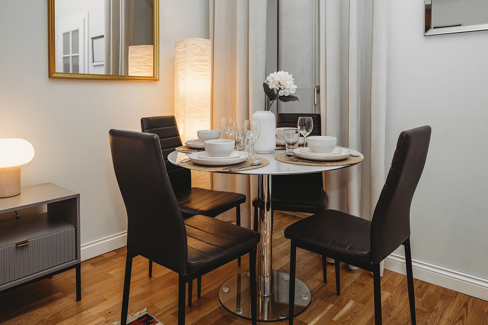 A dining area with a round table, black chairs, white plates, and a vase with flowers.