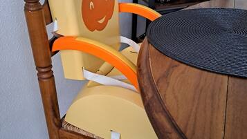 A wooden chair with a cushion and a face design, a round table, and a coffee maker on a shelf.