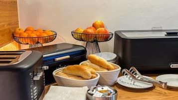 A breakfast setup with a toaster, bread, fruits, and a kettle.