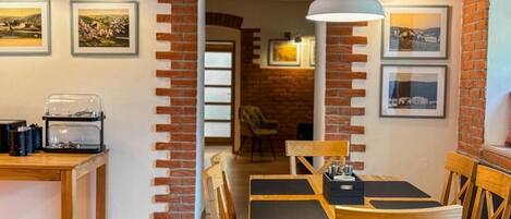 A dining area with brick arches, wooden tables, and chairs. There are framed pictures on the walls and a coffee machine on the table.