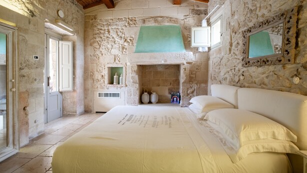 A stone-walled bedroom with a bed, a fireplace, and a window.
