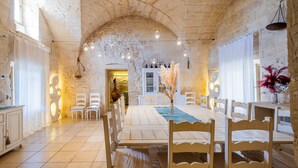 A spacious dining area with a long table, white chairs, and a stone wall.