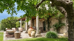 A covered outdoor seating area with wicker furniture, stone pillars, and large vases.