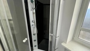 Eine begehbare Duschkabine mit Bedienfeld, einer weißen Ablagefläche und einem Fenster.