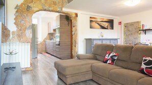 Un salon avec une arche en pierre, un canapé d’angle et une cuisine en arrière-plan.